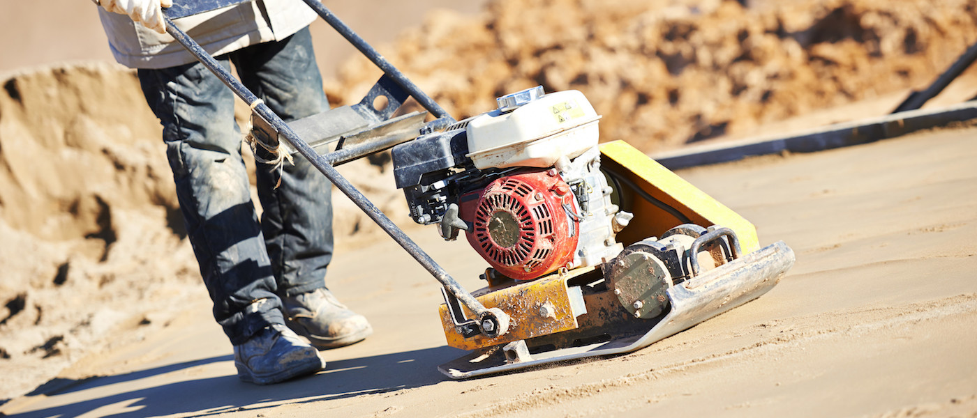 Portable gas powered tamper machine compacting sand to prepare for concrete pour and being operated by worker