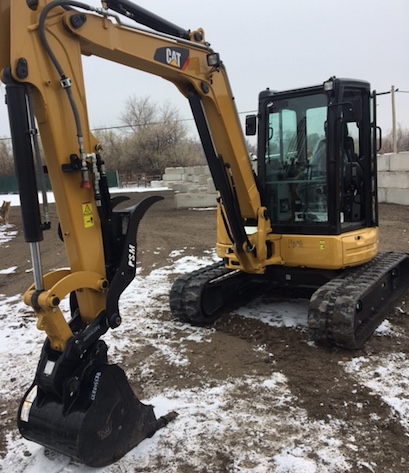 Excavating CAT backhoe sitting in dirt covered with light snow getting ready to excavate