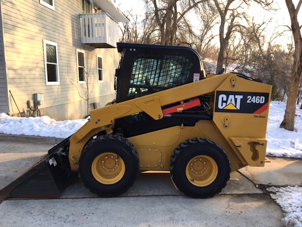 direct side view of a CAT 4-wheeled bobcat excavator sitting on driveway with bucket down