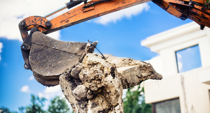 demolition backhoe bucket carrying large concrete debris chunk