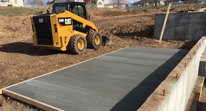 Newly poured concrete pad on residential construction site with bobcat in back