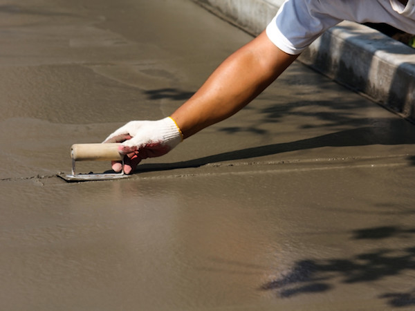 freshly poured concrete being smoothed (screeded) by worker with small trowel one hand and only arm and hand shown