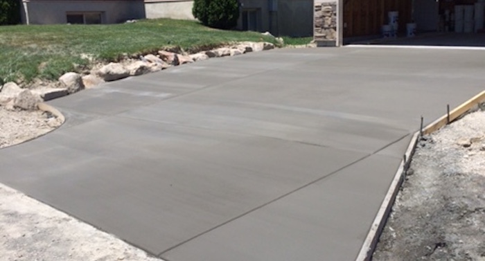 freshly poured and finished cement driveway leading to a residential two car garage with concrete forms still in place