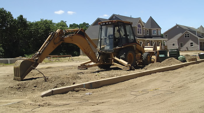 excavating backhoe digging in residential street with finished homes in background